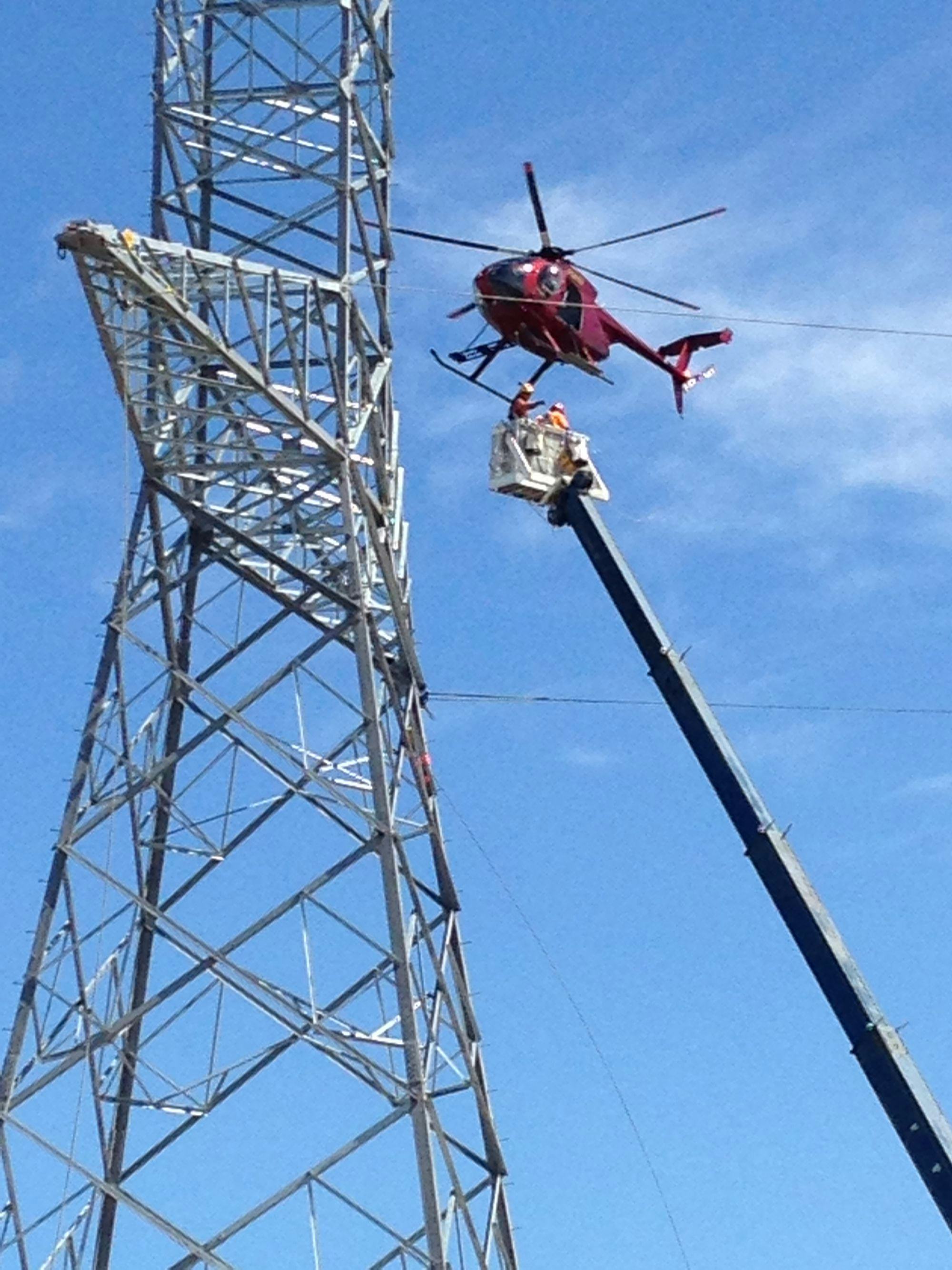 Two men and a red helicopter next to the head of a transmission tower